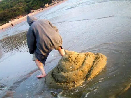 Person standing over giant pile of sand sculpted to look like a turd, so it looks like they pooped it out